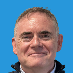 Dr Patrick Murray-Hayden smiling in a professional headshot against a bright blue background.